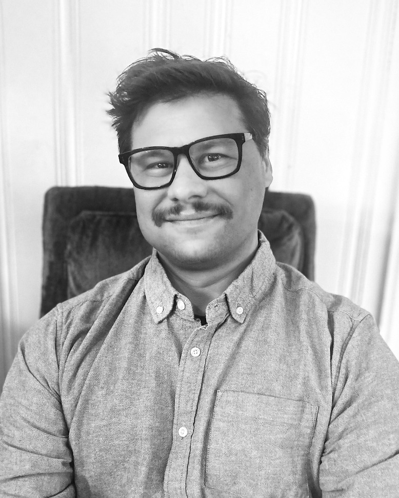 Ryan Micklos smiling in dark-framed glasses and a cardigan